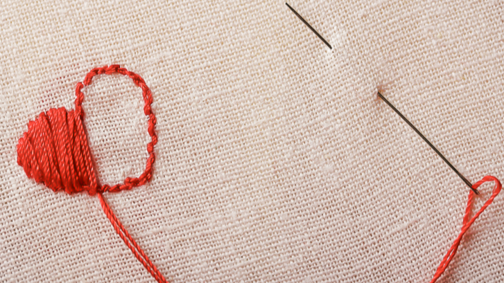 Red thread and needle on beige fabric