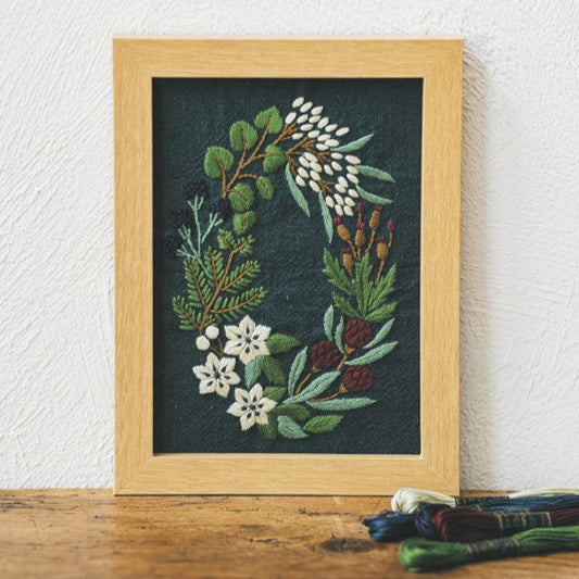 Framed embroidered artwork of flowers and leaves on a wooden surface with a white wall background.